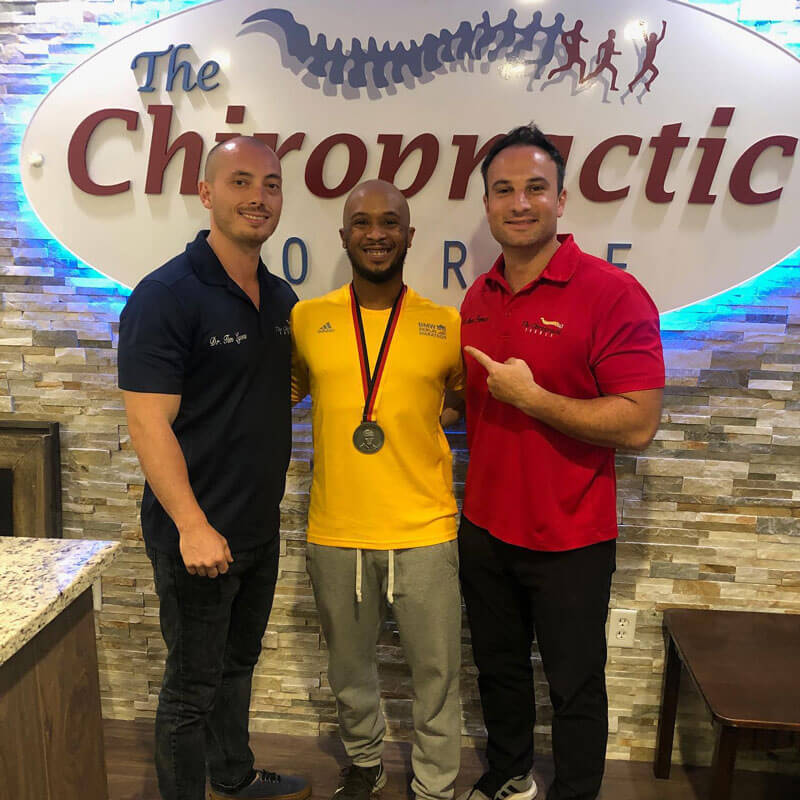 Dr. Marco Ferrucci (left) and Dr. Tim Lyons (right), chiropractors at 'The Chiropractic Source' clinic, posing with a medal-winning athlete in the middle.