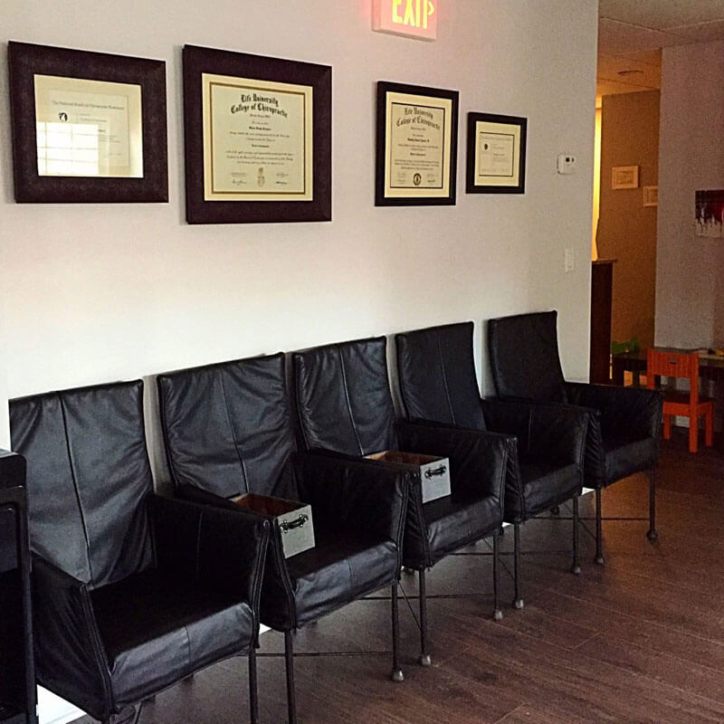 Waiting area at 'The Chiropractic Source' with framed certifications on the wall.