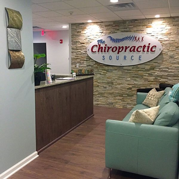 Reception area of 'The Chiropractic Source' clinic with a stone accent wall and branded signage.
